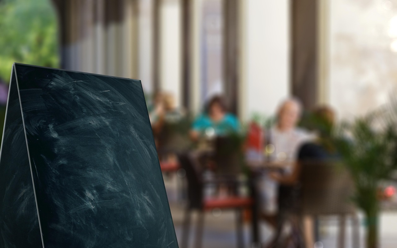 Leere Kreidetafel-Aufstellerkarte vor einer Café-Terrasse — Sinnbild für die täglich aktuelle Speisekarte
